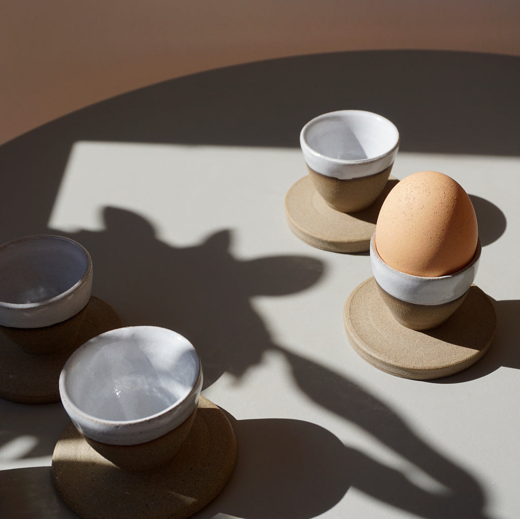 handmade ceramic egg cups on a blue table with an egg in one of them. 
