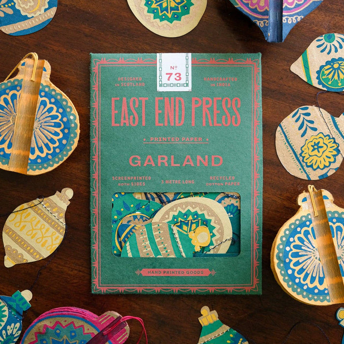Book titled 'Garland' by East End Press surrounded by decorative paper ornaments on a wooden surface. | East End Press | Shop Fodder