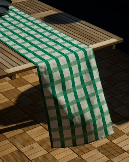 A green and white checkered table runner draped over a wooden slatted table on a wooden deck.
