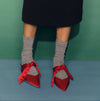 Red shoes with ribbons worn by a person against a green and blue background | Pairs Socks | Shop Fodder