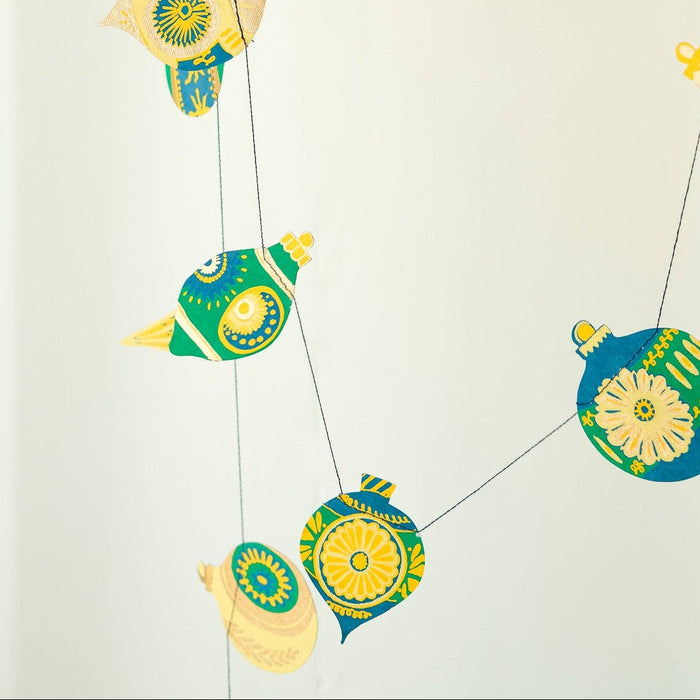 Decorative string with colorful ornaments held by a hand wearing a yellow sweater | East End Press | Shop Fodder