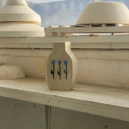 Ceramic vase with floral design on a wooden surface, with pottery in the background. | Tulip Vase | Nerikomi | Fern Taylor | Shop Fodder