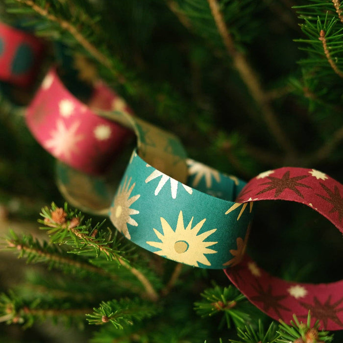 Decorative paper chains with sun and star patterns hanging on a Christmas tree. East End Press | Shop Fodder