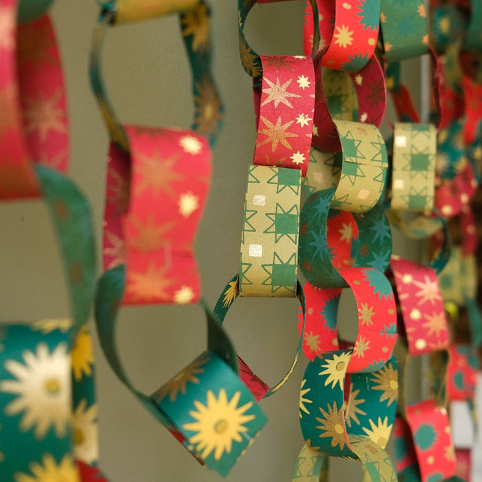 Colorful paper chain with star and sun patterns held by a hand against a neutral background. East End Press | Shop Fodder