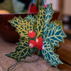 Decorative holly leaf ornament with red berries on a wooden surface. East End Press | Shop Fodder