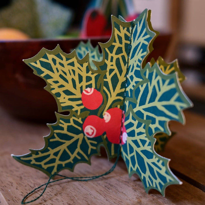 Decorative holly leaf ornament with red berries on a wooden surface. East End Press | Shop Fodder