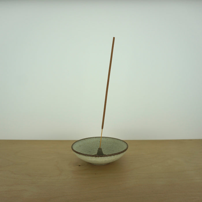 a simple and elegant incense holder with a stick of incense on a table. 