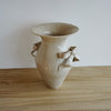 Beige ceramic vase with decorative handles on a wooden surface. Amelia Christoffers | Shop Fodder