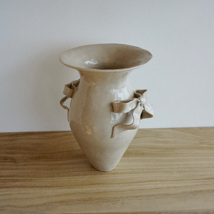 Beige ceramic vase with decorative handles on a wooden surface. Amelia Christoffers | Shop Fodder
