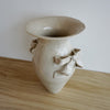 Beige ceramic vase with bow decorations on a wooden surface.  Amelia Christoffers | Shop Fodder