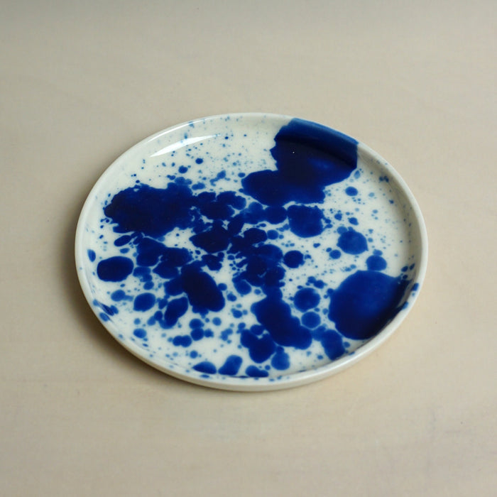 Ceramic plate with blue splatter design on a beige background. Splatter Saucer | Anna Jones Ceramics | Shop Fodder