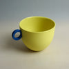 Yellow cup with a blue handle on a neutral background. Syros Mug | Anna Jones Ceramics | Shop Fodder