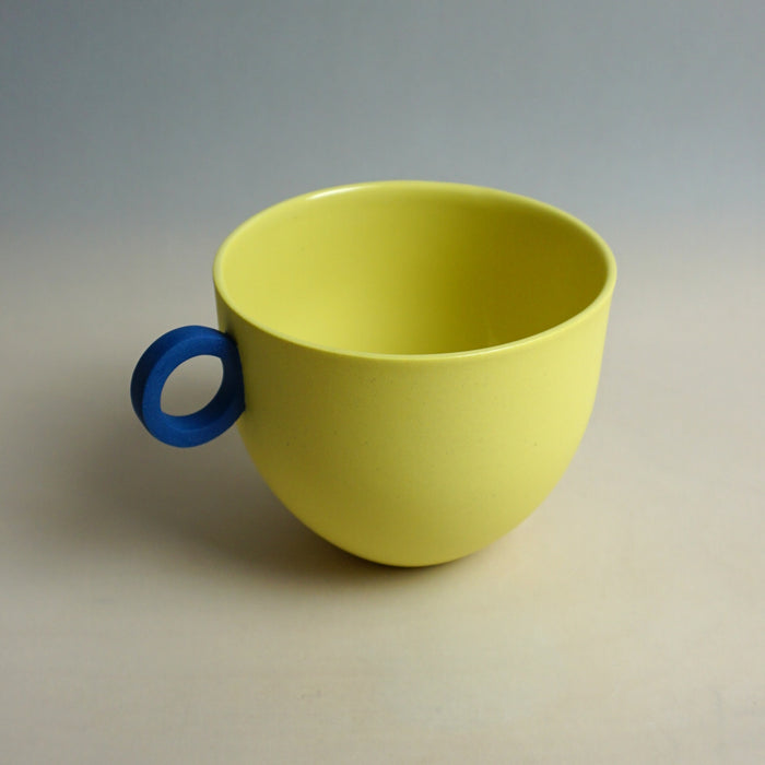 Yellow cup with a blue handle on a neutral background. Syros Mug | Anna Jones Ceramics | Shop Fodder