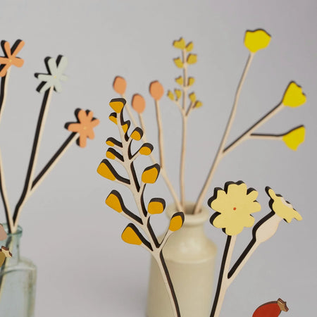 Decorative floral branches with yellow and orange flowers in a vase against a plain background. Anna Wiscombe | Shop Fodder