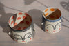 a black planter and a blue planter in the sunshine. faces painted on the outside and red and orange dots on the inside. 
