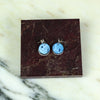 Pair of blue earrings on a brown marble surface. Scarlett Cohen French | Shop Fodder