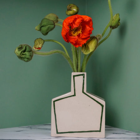 Angular vase with green outline and red poppies on a marble table and a green background. 