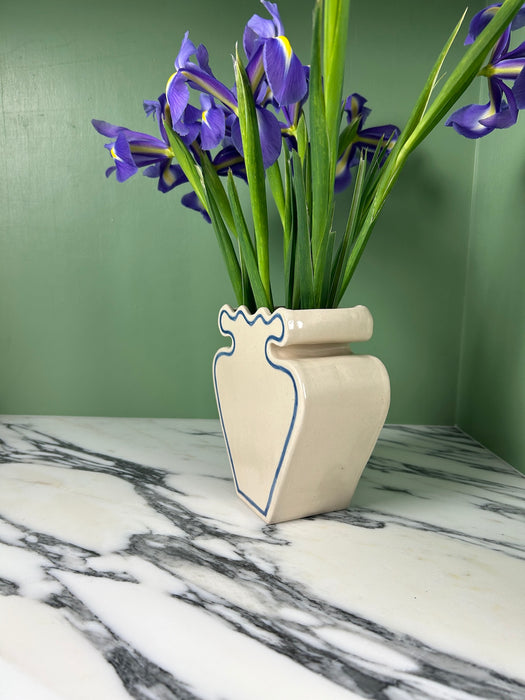 side view of a cream vase with blue outline pattern and a bunch of iris on a green background