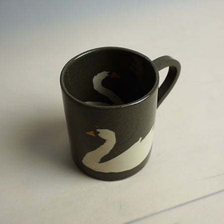 Black mug with a white swan design on a light backgroundTwo brown mugs with white swan designs on a light grey background | Fern Taylor Ceramic Nerikomi Vase | Shop Fodder