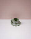 Green ceramic cup and saucer on a white surface with a pink background. Portrait Mug | Brutes London | Handmade Ceramics | Fodder