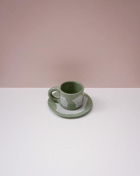 Green ceramic cup and saucer on a white surface with a pink background. Portrait Mug | Brutes London | Handmade Ceramics | Fodder