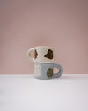 Two ceramic mugs stacked on a white surface with a pink background. Portrait Mug | Brutes London | Handmade Ceramics | Fodder