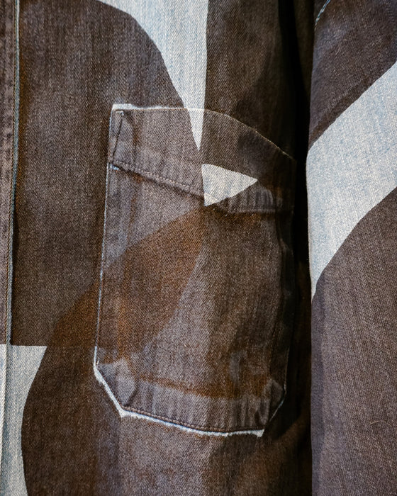 Close-up of a brown denim jacket featuring a large chest pocket with a unique triangular stitched detail, set against a matching abstract geometric patterned fabric. Caroline Dickinson Shirt | Fodder
