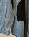 Close-up of a light blue denim jacket featuring a large black fabric patch on the chest. Caroline Dickinson Shirt | Fodder