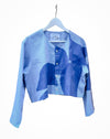A cropped long-sleeve button-up shirt in a light blue denim-like fabric, featuring an abstract geometric pattern in various shades of blue. The shirt is displayed on a white hanger against a plain white background. Caroline Dickinson Shirt | Fodder