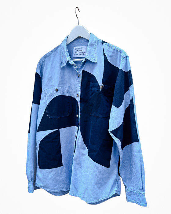A long-sleeve button-up shirt with a light blue and dark navy blue patchwork design, hanging on a white hanger against a plain white background. Caroline Dickinson Shirt | Fodder