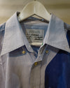 A close-up of a Caroline Dickinson shirt on a white hanger, featuring a blue and white striped pattern on the upper chest and a solid dark blue panel on the lower right. Caroline Dickinson Shirt | Fodder