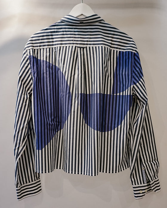 A long-sleeve button-up shirt hanging on a white hanger against a plain light background. The shirt features a black and white vertical stripe pattern with large blue abstract circular patches on the back. Caroline Dickinson Shirt | Fodder
