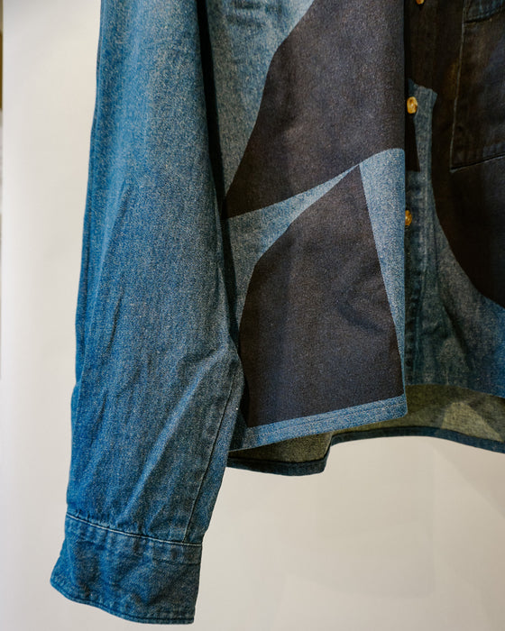 A close-up of a long-sleeve button-up shirt featuring a geometric patchwork pattern of blue denim and dark charcoal grey fabric panels, with gold buttons. Caroline Dickinson Shirt | Fodder