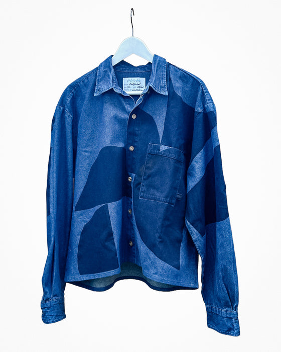 A blue patchwork patterned long-sleeve button-up shirt hanging on a white hanger against a plain white background. Caroline Dickinson Shirt | Fodder