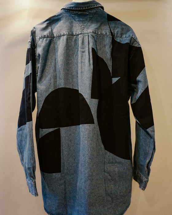 A long-sleeve denim shirt shown from the back, featuring a large abstract black geometric patchwork pattern over a light blue denim base. Caroline Dickinson Shirt | Fodder