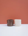 Two textured ceramic planters, one dark brown and one off-white, displayed side-by-side on a white surface against a terracotta-colored background. Brutes Ceramics | Hope Collection | Shop Fodder