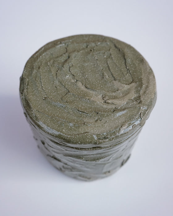 A cylindrical jar filled with a thick, textured gray-green cream or balm, photographed from a top-down angle on a plain white background. Brutes Ceramics | Hope Collection | Shop Fodder