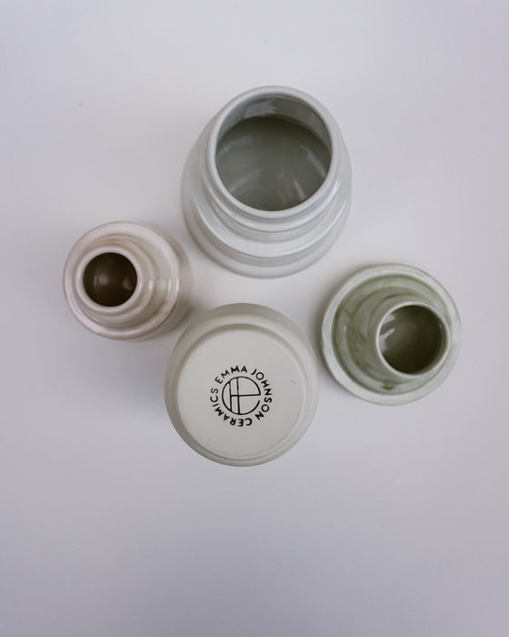 Four small ceramic jars with matching lids arranged on a plain white background. One jar is open at the top, one lid is shown upside down with a visible circular logo reading 'ESMA JOHAN CEBANCI' and 'CEMENT', one lid is off showing the inside, and one jar is partially open.  Emma Johnson Ceramics | Fodder | Hope Collection