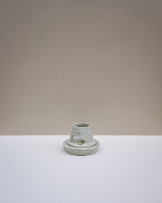 A small light green ceramic candle holder with a matching saucer, centered on a white surface against a warm beige background. Emma Johnson Ceramics | Fodder | Hope Collection