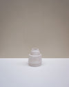 A small ceramic vase with a textured, matte finish in a light off-white color, set on a white surface against a neutral beige background. Emma Johnson Ceramics | Fodder | Hope Collection