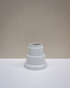 A small white ceramic vase with a tiered, stepped design, set on a white surface against a warm beige background. Emma Johnson Ceramics | Fodder | Hope Collection