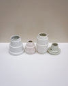Four small ceramic vases in different glazes and shapes arranged on a white surface against a warm beige. Emma Johnson Ceramics | Fodder | Hope Collection