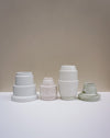 Four matte ceramic pots in different colors and sizes arranged on a white surface against a warm beige.  Emma Johnson Ceramics | Fodder | Hope Collection