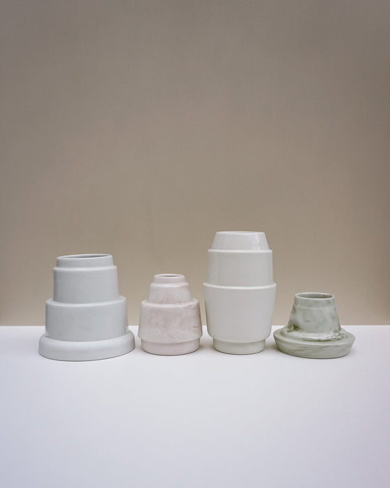 Four matte ceramic pots in different colors and sizes arranged on a white surface against a warm beige.  Emma Johnson Ceramics | Fodder | Hope Collection