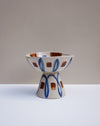 A ceramic pedestal bowl with a geometric pattern of blue ovals and brown squares on a white base, set against a neutral beige and white  Hoodmor Studio | Fodder | Hope Collectionbackground.