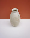 A small handmade ceramic vase with a speckled cream glaze and a subtle hand-painted floral motif on the front, set against a split orange and white background. KJA Studio Ceramics | Hope Collection | Shop Fodder