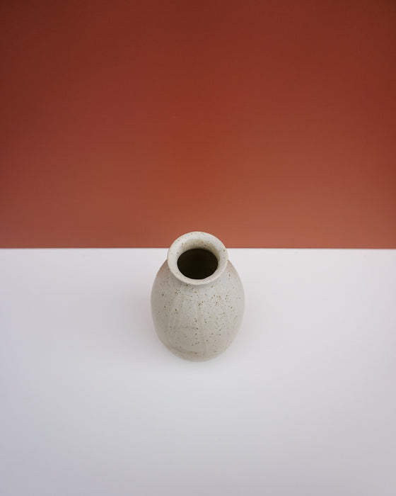 A small speckled ceramic vase with a wide opening, standing on a white surface against a terracotta-colored background.  KJA Studio Ceramics | Hope Collection | Shop Fodder
