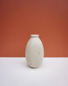 A small speckled ceramic vase with a flared rim and subtle leaf embossing, standing on a white surface against a terracotta-colored background. KJA Studio Ceramics | Hope Collection | Shop Fodder