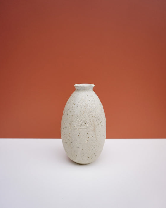 A small speckled ceramic vase with a flared rim and subtle leaf embossing, standing on a white surface against a terracotta-colored background. KJA Studio Ceramics | Hope Collection | Shop Fodder