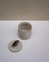A handmade ceramic jar with its lid off, showing a small bird figurine inside. The jar has a light gray glaze with a rustic brown rim, and the lid is off to reveal the bird. Liz Vidal Ceramics | Fodder | Hope Collection